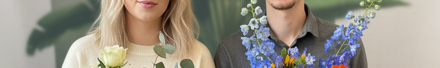 Zwei Personen sitzen nebeneinander und halten Blumensträuße in den Händen, im Hintergrund steht eine große grüne Zimmerpflanze.